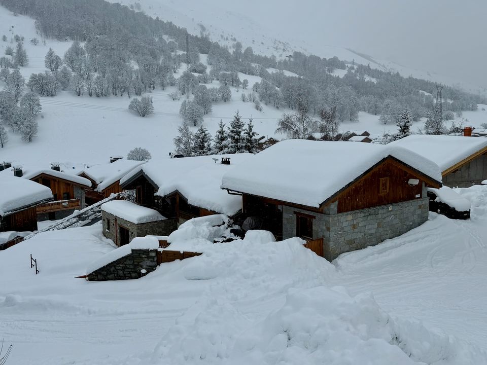 Chalet Gabriel after a heavy fall — the roof holds a metre of snow, and the road past the door is cleared by morning.